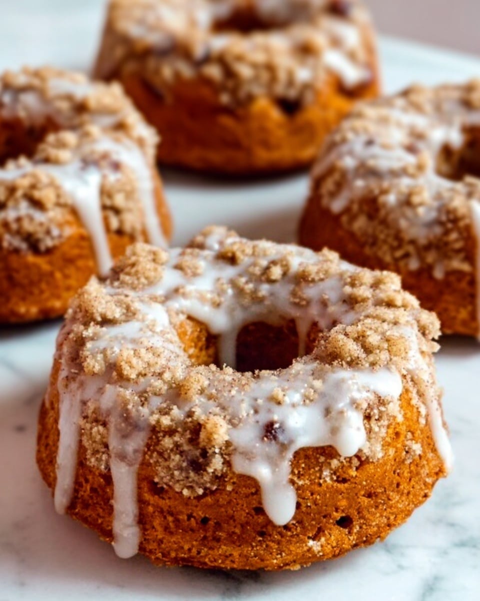 The image shows eight round donuts with a rough, crumbly texture on top, covered with a light drizzle of white icing, arranged neatly in two rows on a white rectangular plate. Each donut has a golden-brown base layer with a slightly uneven surface topped by a thick layer of crumbly streusel in a light brown color that adds a crunchy texture. The white icing drips unevenly over the crumbs, creating thin streaks that contrast with the warm tones of the donut. The plate is set on a white marbled surface, adding a clean and bright backdrop to the warm, textured donuts. photo taken with an iphone --ar 4:5 --v 7