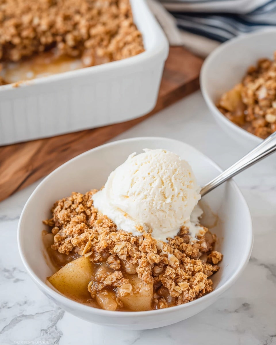 A close-up of a white baking dish filled with a baked apple crumble dessert, showing two main layers: the bottom layer is soft, cooked apple pieces in a light brown syrup, and the top layer is a golden brown, crunchy crumb topping with a grainy texture. A spoon holds a scoop of the crumble above the dish, with visible chunks of apple and crisp, crumbly topping. The dish sits on a white marbled texture surface. photo taken with an iphone --ar 4:5 --v 7