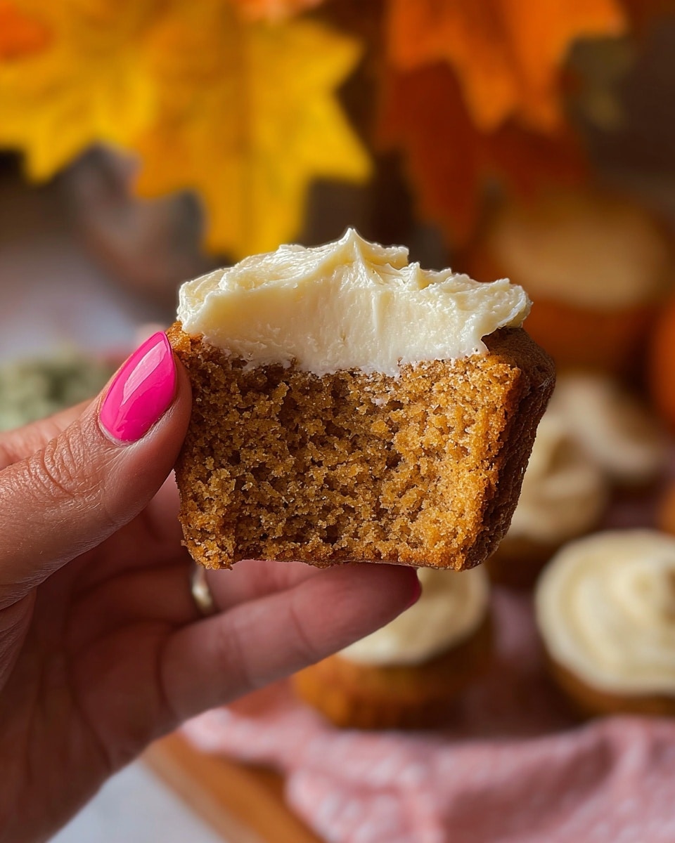 A close-up of a woman's hand with pink painted nails holding a split cupcake against a soft-focused background of warm yellow and orange leaves. The cupcake consists of two layers: the bottom layer is a moist, crumbly, light brown cake with visible air pockets, and the top layer is a thick, creamy white frosting with a fluffy texture. The scene has a cozy autumn feel, highlighted by the soft natural light. Photo taken with an iphone --ar 4:5 --v 7