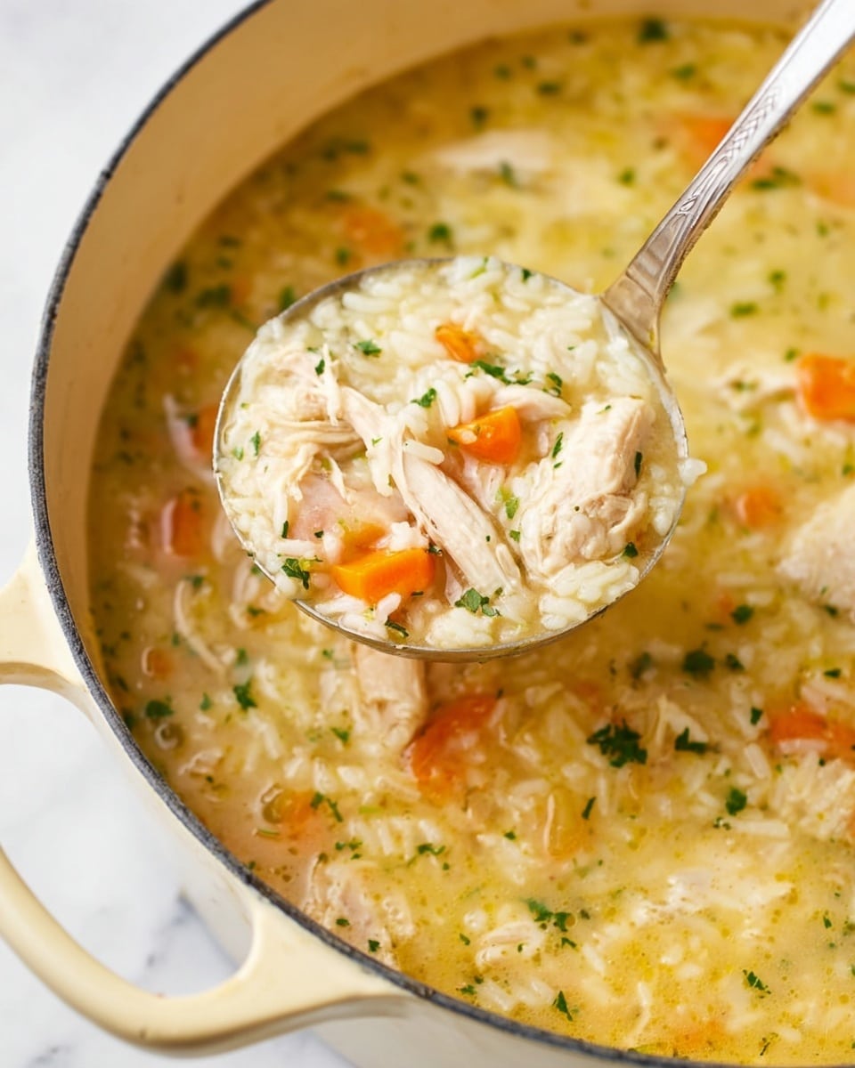 A white speckled bowl full of chicken and rice soup sits on a white marbled surface. The soup has a creamy light yellow broth rich with visible cooked rice and thin strips of white shredded chicken. Bright orange slices of carrot float throughout, while small bits of green parsley are sprinkled on top, adding color contrast. A gold spoon rests inside the bowl on the right side, partially submerged in the soup. The textures of the broth look smooth yet hearty with the soft rice and chicken pieces visible. photo taken with an iphone --ar 4:5 --v 7