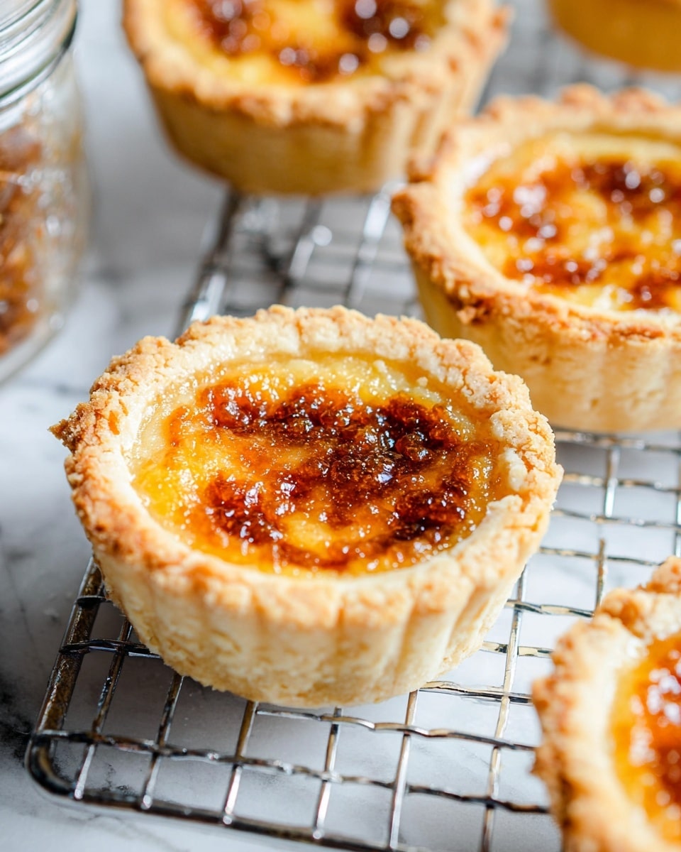 A close-up view of small tartlets with a crumbly, pale golden crust forming the bottom and sides. The crust has a slightly rough texture with visible cracks and uneven edges. Each tartlet is filled with a caramelized, bubbly filling that is golden brown with darker, almost burnt spots scattered across the surface, giving a rich, glossy appearance. The tartlets are placed on a metal cooling rack over a white marbled surface, with some parts of a glass jar and more tartlets softly blurred in the background. photo taken with an iphone --ar 4:5 --v 7