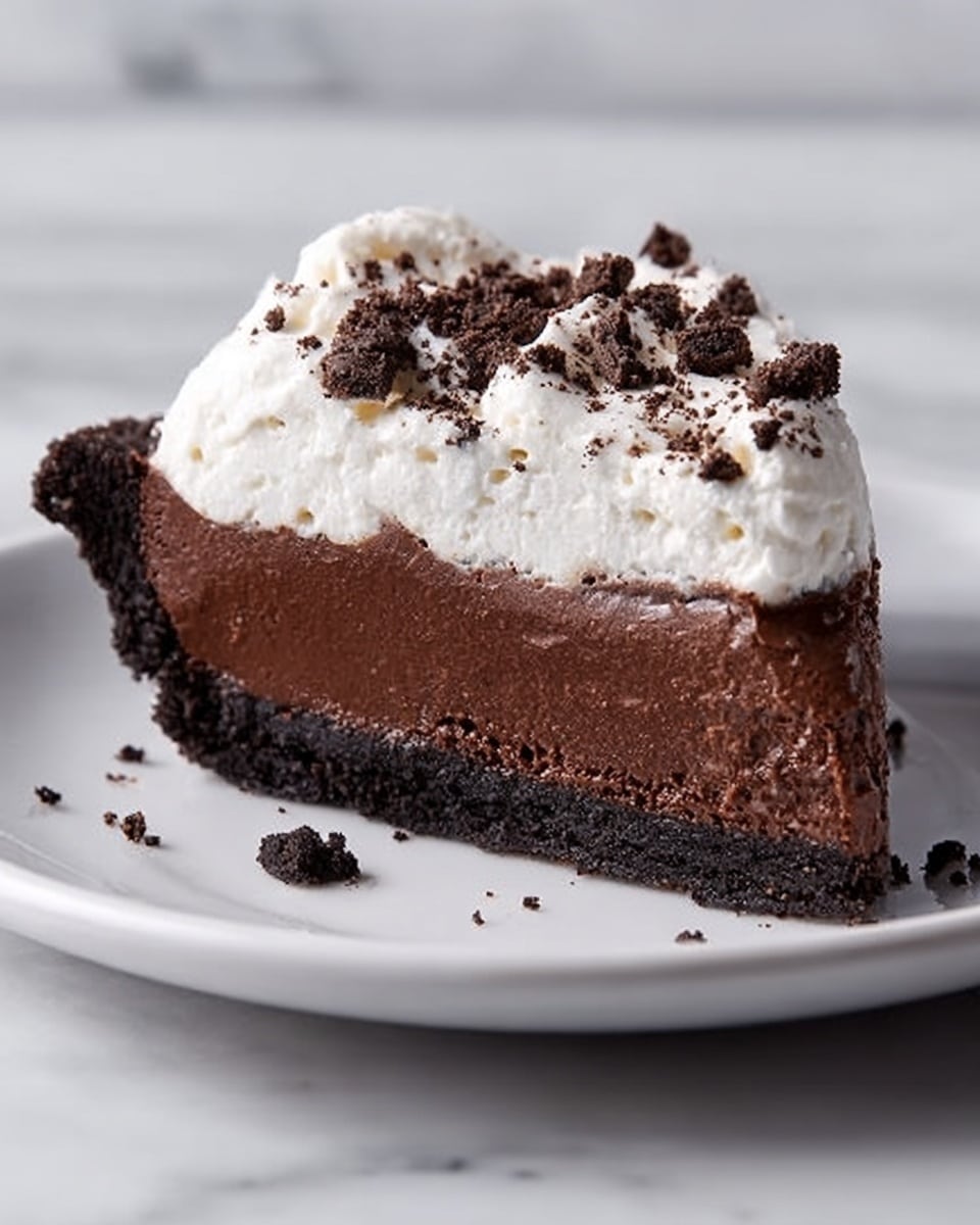 A slice of rich chocolate pie with three visible layers is placed on a white plate on a white marbled surface. The bottom layer is a dark, crumbly crust made of crushed cookies. Above it is a thick, smooth, and shiny dark brown chocolate filling that looks creamy and dense. The top layer is a fluffy white whipped cream, thickly spread and slightly uneven. Crumbled cookie pieces are sprinkled over the whipped cream, adding texture and contrast. Photo taken with an iphone --ar 4:5 --v 7