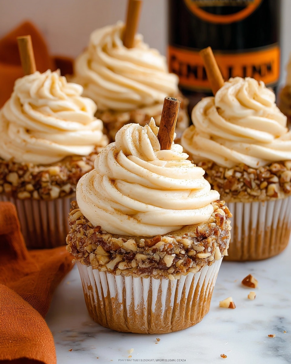 The image shows multiple cupcakes, each with one main layer of light brown cake in a white paper liner. On top, there is a thick layer of cream-colored frosting with chopped nuts pressed onto its sides, adding a rough texture and darker brown color. Each cupcake is topped with a generous swirl of smooth, creamy frosting in a light beige color. One cinnamon stick is placed vertically into the frosting on each cupcake, giving a warm brown contrast. The cupcakes sit on a white marbled surface with an orange cloth underneath and a partially visible black can with orange lettering in the background. photo taken with an iphone --ar 4:5 --v 7