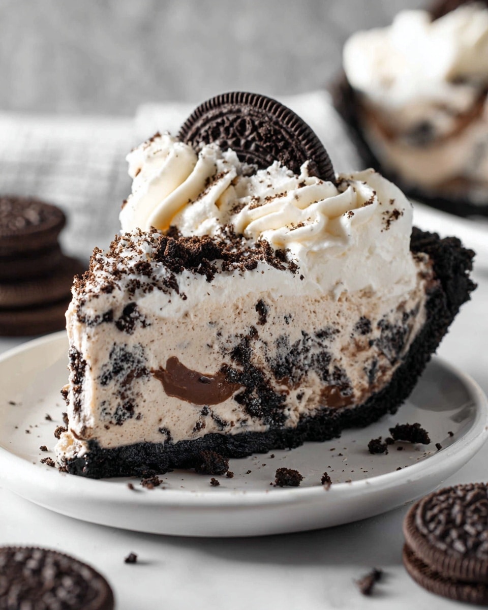 A slice of cookies and cream pie sits on a white plate with a white marbled surface background. The pie has three visible layers: a dark, crumbly chocolate crust at the bottom; a thick, creamy filling mixed with crushed dark cookie chunks in the middle; and a smooth, white whipped cream topping with fine crushed cookie bits sprinkled on top. A swirl of whipped cream decorated with half a dark chocolate cookie is on the top center of the slice. In the foreground, whole chocolate cookies are partially visible. photo taken with an iphone --ar 4:5 --v 7