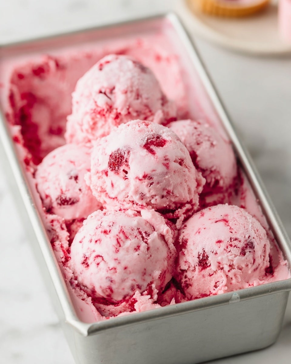 The image shows a metal rectangular container filled with pink ice cream that has red fruit pieces mixed inside. There are six rounded scoops of ice cream placed on top, with a creamy, slightly chunky texture. The ice cream looks soft and smooth with visible bits of red fruit spread evenly. The container is set on a white marbled surface, and parts of the ice cream slightly overflow the edges. The background is softly blurred, keeping the focus on the vibrant pink ice cream. photo taken with an iphone --ar 4:5 --v 7