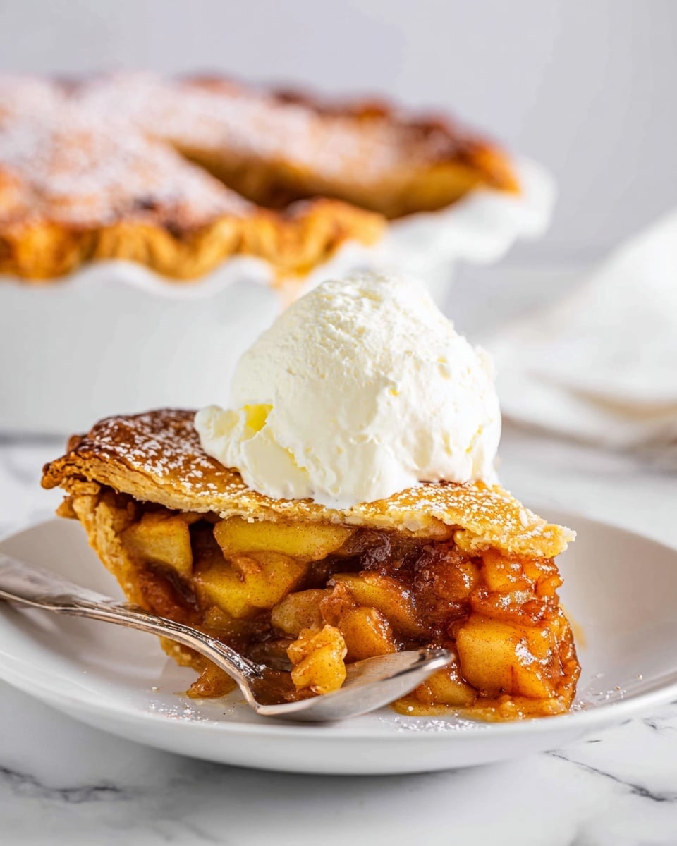 The image shows a close-up of a golden-brown baked pastry with a slightly uneven surface and light textures of cinnamon and sugar on top, sitting on a white floral patterned plate. Next to the pastry, there are two scoops of smooth, creamy vanilla ice cream, which have small dark specks indicating real vanilla bean. In the background, a blurred red apple and a white baking dish with more pastries can be seen, all set on a white marbled surface. The lighting highlights the warm, inviting colors of the dessert and ice cream. photo taken with an iphone --ar 4:5 --v 7