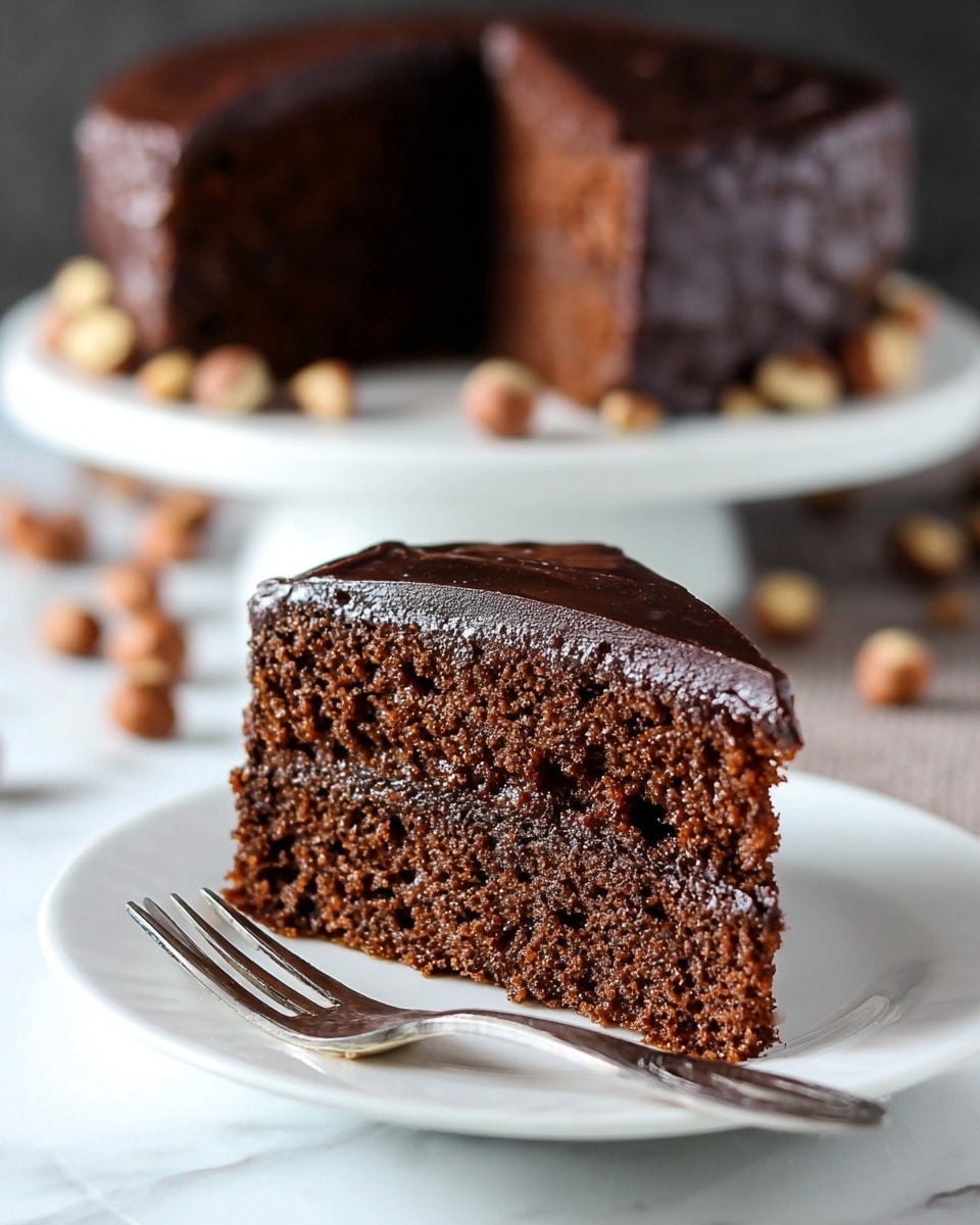 A close-up of a tall slice of cake with three main layers: at the bottom and middle, there are two thick, soft brown cake layers, and between them is a thick layer of light beige frosting mixed with small bits of crushed nuts or caramel pieces. The top layer is made of the same light beige frosting, swirled and textured with soft peaks, sprinkled lightly with crumbs. A piece of milk chocolate candy with tiny bits on its surface stands upright on top. The slice sits on a white plate with some crumbs scattered around, on a white marbled surface. photo taken with an iphone --ar 4:5 --v 7