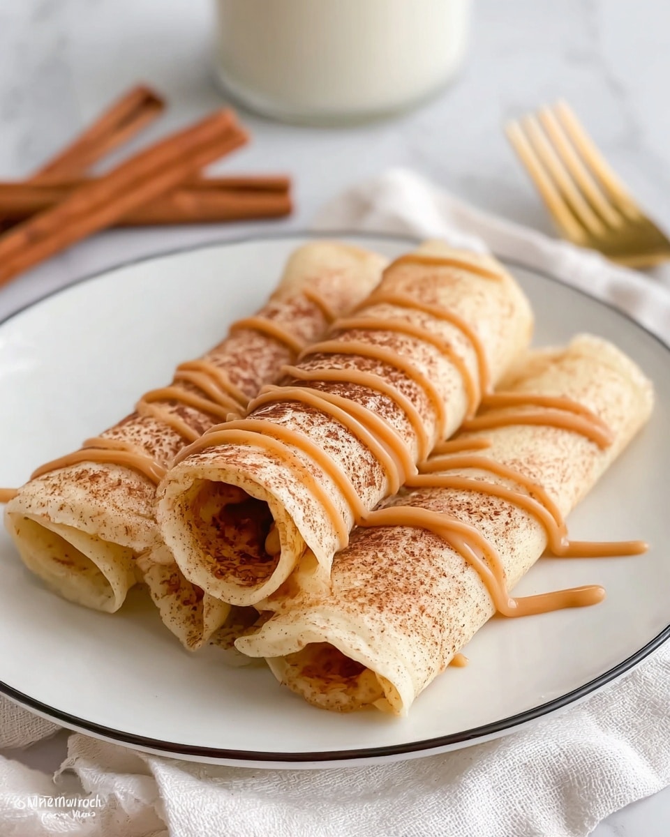 Three light beige crepes are rolled up and stacked in a triangle shape on a white plate with a thin black rim. The crepes have a dusting of light brown cinnamon powder on top and are drizzled in a wavy pattern with smooth, glossy caramel sauce. Behind the plate, a glass of milk and a few cinnamon sticks are visible on a white marbled surface, adding to the cozy feel. A gold fork lies nearby on a white cloth, and a woman's hand is just out of frame, suggesting someone is about to enjoy the dish. Photo taken with an iphone --ar 4:5 --v 7