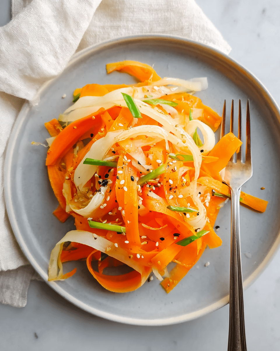 A white plate filled with thin ribbons of orange and pale yellow vegetables, likely carrot and daikon, arranged loosely in layers with some overlapping curls and folds. The orange ribbons are bright and smooth, while the pale yellow ones have a slightly translucent texture. Small green pieces, possibly scallions, are scattered on top along with white and black sesame seeds. A silver fork rests on the right side of the plate. The plate is placed on a white marbled surface with a light cream cloth partially visible in the background. Photo taken with an iphone --ar 4:5 --v 7