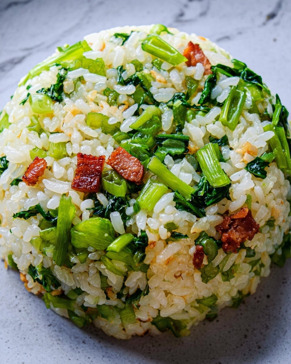 A close-up view of a dome-shaped serving of rice mixed with green vegetable pieces and small crispy brown slices of meat, all tightly packed together. The rice looks soft and sticky with slightly shiny white grains. The green vegetable pieces are bright and fresh, scattered evenly throughout the rice. The crispy meat slices are golden-brown with a slightly shiny texture, peeking out from the rice mixture. The dish sits on a flat surface with a white marbled texture in the background. photo taken with an iphone --ar 4:5 --v 7