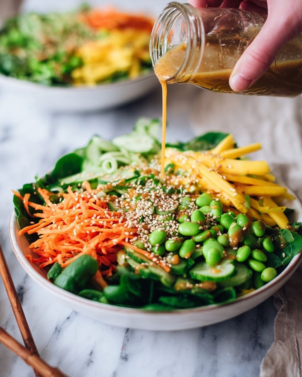 A white shallow bowl filled with a fresh salad made of several layers: the base layer has dark green leafy spinach, the next layer includes bright orange shredded carrots and yellow mango strips, topped with light green edamame beans and sliced cucumber rounds scattered on top. A sprinkle of white sesame seeds is spread over the salad. Above the bowl, a woman's hand holds a small glass jar pouring a light brown dressing over the salad. In the background, there is another similar white bowl with a salad sitting on a white marbled surface with a pair of wooden chopsticks beside the foreground bowl. photo taken with an iphone --ar 4:5 --v 7