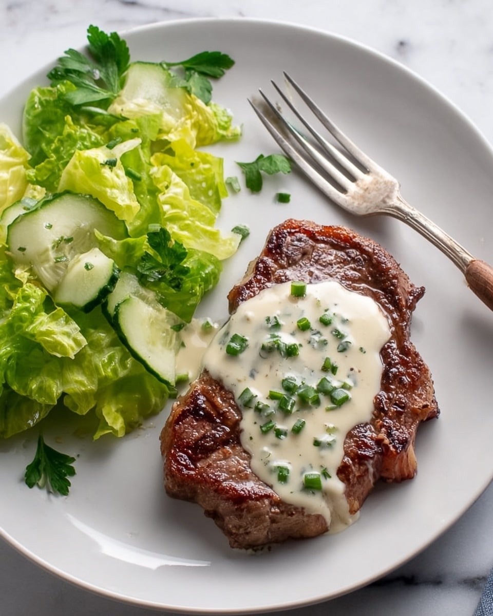 A white plate with a piece of grilled steak on the right side covered with a creamy white sauce topped with small green parsley pieces, the steak has a brown grilled texture with visible sear marks and some pink edges showing; on the left side, there is a small fresh salad made of green lettuce leaves and cucumber slices, both the lettuce and cucumber are light green and crisp; a fork is placed above the steak with some parsley nearby, the plate is set on a white marbled surface in soft natural light, photo taken with an iphone --ar 4:5 --v 7