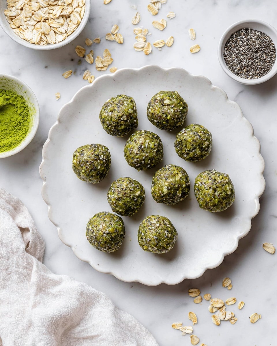 The image shows a white scalloped plate holding eleven green energy balls arranged loosely in two rows and a small third row. Each ball has a rough texture with visible oats and chia seeds mixed in, giving a slightly shiny and dense look. Around the plate on a white marbled surface are scattered oats and two small white bowls, one filled with bright green powder and the other with chia seeds, adding context to the ingredients. A white cloth is partially draped near the top left corner of the plate. photo taken with an iphone --ar 4:5 --v 7