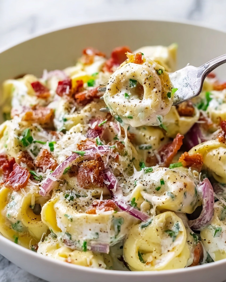 A close-up view of creamy tortellini pasta layered in a white bowl, each tortellini filled and coated in a rich white sauce with a smooth texture. Scattered over the pasta are crispy reddish-brown bacon pieces, thin purple onion slices, and bright green chopped herbs, adding pops of color. The pasta is lightly sprinkled with finely grated white cheese and cracked black pepper for texture on top. A silver fork is lifting a piece of the tortellini, showing its creamy filling and the sauce dripping softly. The bowl is placed on a white marbled surface. photo taken with an iphone --ar 4:5 --v 7