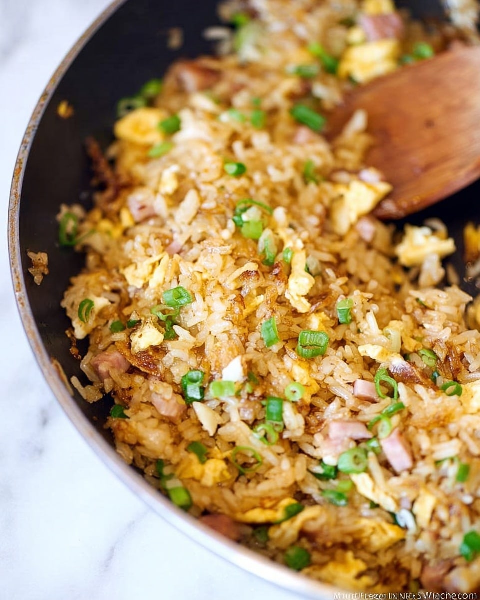 A close-up of a skillet showing a mixture of fried rice with visible pieces of scrambled eggs, green onions, and small chunks of light pink ham. The fried rice is golden brown with some bits slightly crispy, giving a textured look. Scattered green onion pieces add splashes of green throughout the dish. A wooden spoon is partially visible on the right side, resting inside the skillet. The whole scene is set on a white marbled surface. photo taken with an iphone --ar 4:5 --v 7