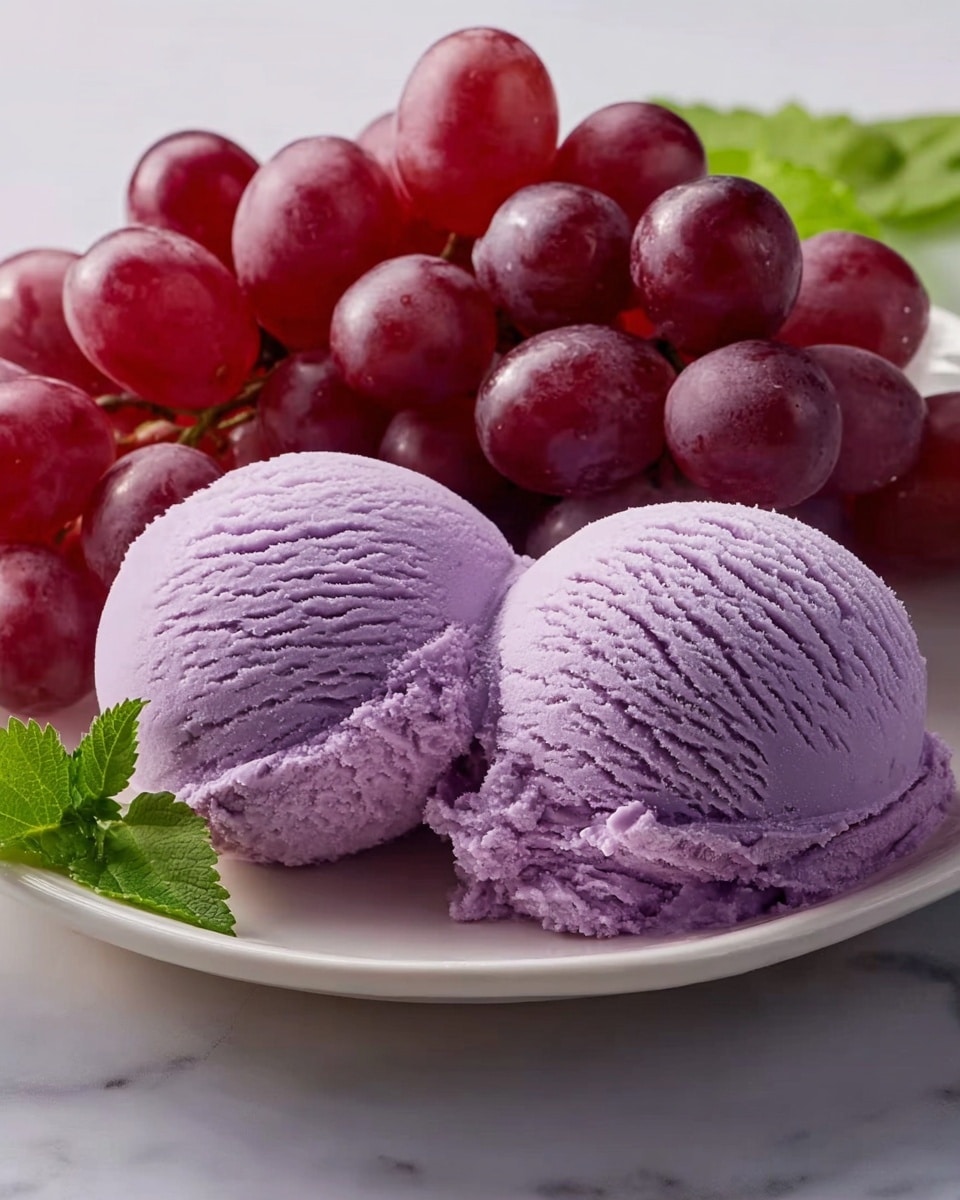 The image shows two scoops of smooth, light purple ice cream placed side by side on a white plate, with visible texture lines from scooping. Next to the ice cream, there is a bunch of shiny, dark red grapes with a glossy surface and a small green leaf on the left corner of the plate. The plate rests on a white marbled surface, creating a clean and bright background. photo taken with an iphone --ar 4:5 --v 7