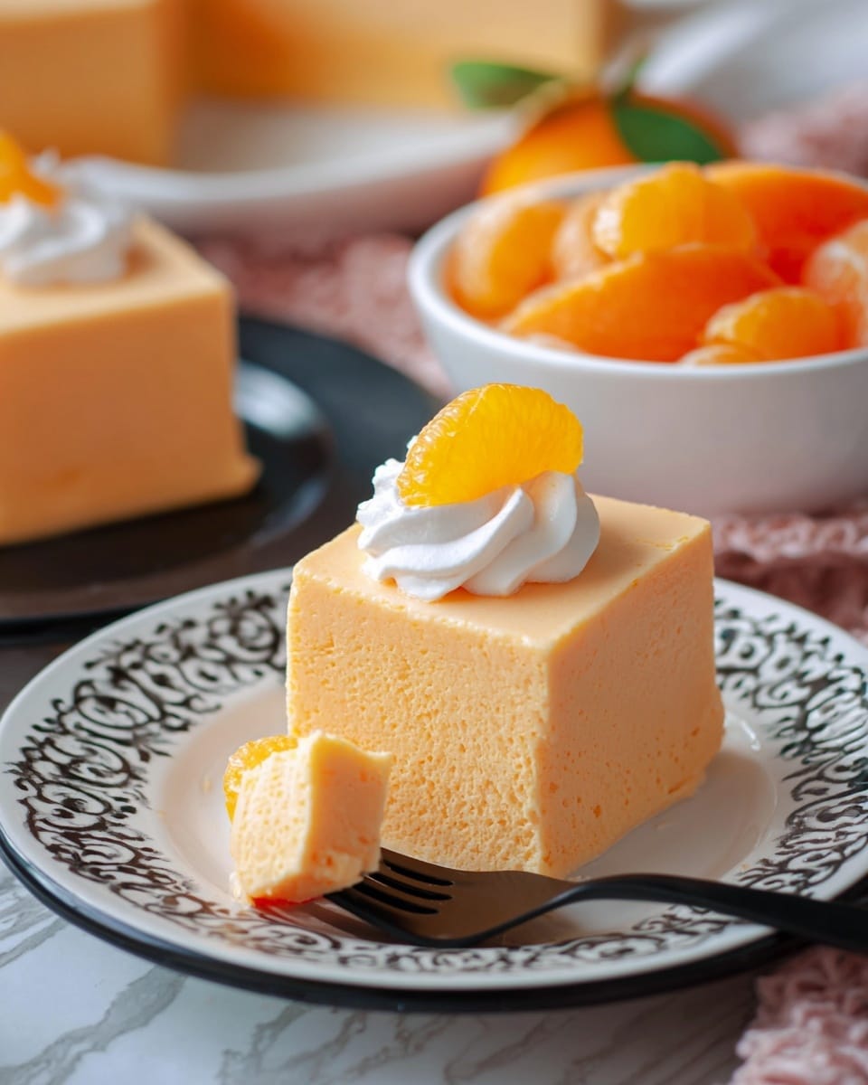 A square piece of light orange mousse-like dessert sits on a white plate with black decorative edges, showing one clean bite taken from its front side to reveal a smooth and soft texture. On top of the dessert is a small swirl of white whipped cream and a bright orange mandarin slice. A black fork holds a cut piece of the dessert in the foreground. In the background, there is a white bowl filled with more mandarin slices and another piece of the same dessert on a black plate, all placed on a white marbled surface. photo taken with an iphone --ar 4:5 --v 7